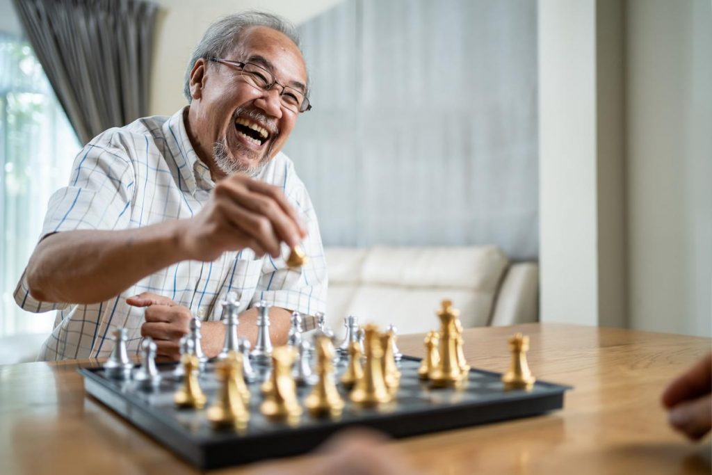 Mature man laughs as he moves his chess piece during a game